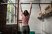 Young woman exercising in gym, hanging from bar