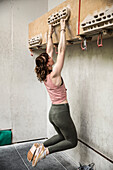 Young woman hanging from training board at climbing center