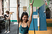 Happy woman exercising at gymnastics rings in gym
