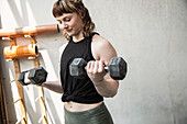 Young woman weightlifting with dumbbells in gym