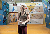Young female rock climber looking up in climbing gym