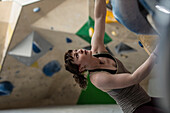 Young female rock climber looking up at climbing wall