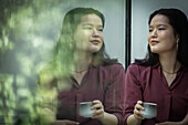 Thoughtful young woman drinking tea at window