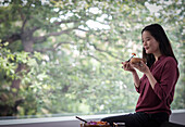 Young woman eating with chopsticks at window