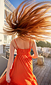 Woman in orange dress flipping long red hair