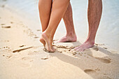 Bare feet of couple in sand on sunny beach