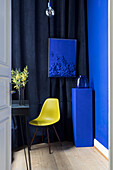 Gelber Stuhl vor dunkelblauem Vorhang im Zimmer mit blauer Wand