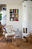 Reading nook with rattan chair next to white tiled stove