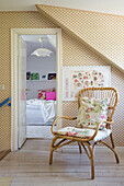 Treppenabsatz mit gemusterter Tapete und Rattanstuhl, Blick ins Schlafzimmer