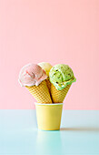 Strawberry, vanilla, and pistachio ice cream in waffle cones against a pink background