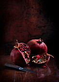 Pomegranates with a kitchen knife on shiny wooden tabletop