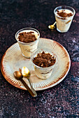 Tiramisu served as individual servings in glasses on ceramic plate and rusted surface