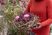 Frau trägt Osternest aus Stroh mit Eiern und rosa Schneeheidenzweige (Erica carnea)