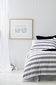 A coastal style bedroom with white panelled walls, a curtain and a white floor