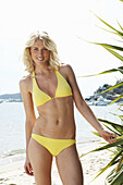 A blonde woman on a beach wearing a yellow bikini