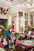 Dining room with lush floral decoration, set table with parrot sculpture as candle holder