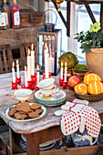 Wooden table with biscuits, dishes, candles, plants, and fruit in the greenhouse