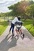 Affectionate mum hugging daughter in rollator at sunny park