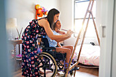 Mum and disabled daughter in wheelchair painting in bedroom