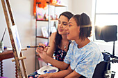 Mother and disabled daughter painting at easel in bedroom