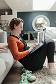Young woman working from home at laptop on living room floor