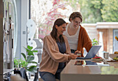 Happy women friends online shopping at laptop in kitchen