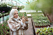 Woman with phone photographing hanging basket in garden shop