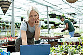 Female garden shop owner talking on smart phone at laptop