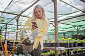 Woman with camera phone shopping for potted flowers