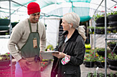 Garden shop owners with clipboard talking in greenhouse