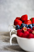 Strawberries, blueberries, and raspberries in small bowls on a concrete background