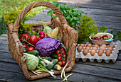 Fresh vegetables in a basket next to herbs, egg pallet and a small bowl with berries