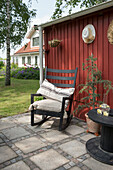 Cozy chair with cushion and side table made of cable drum on patio in front of red-brown house