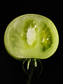 Half a green tomato against a black background