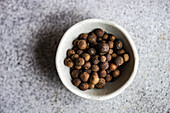 Stone bowl with black pepper spice on concrete background