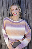 Junge blonde Frau im Strickpullover mit Farbverlauf vor Bretterwand