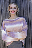 Young blond woman in knitted jumper with colour gradient in front of board wall