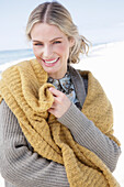 Junge blonde Frau mit gelbem Schal in grauer Strickjacke am Strand