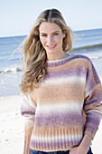 Young blonde woman in a knitted jumper with a colour gradient at the seaside