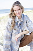 Young blonde woman in checked coat and suede trousers by the sea