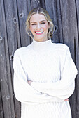 Young blond woman in white knitted jumper in front of board wall