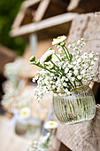 Weisse Blumen in einer Glasvase hängen an einer Holzpalette