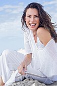 Happy, long-haired woman in white jumper and white trousers on the beach