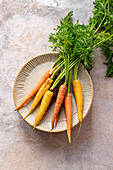 Bunch of colourful organic carrots with greens on a stack of ceramic plates