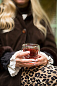 Frau hält ein Glas Tee in den Händen (Teilansicht)