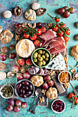 Snack board with different kind of cheese, jamon serrano, fuet, buns, olives, cherry toamtoes, grapes, walnuts, jam and capers