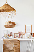 White desk with artwork, rattan armchair, pendant lamp, and dried flowers