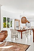 Rustic wooden dining table with white chairs, rattan lamp above in dining room