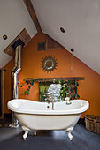 Freestanding bathtub in an attic bathroom with an orange wall