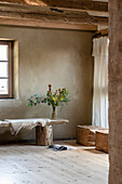 Wooden bench with sheepskin as table and leather square pouf in a room with clay plaster wall and wooden beams